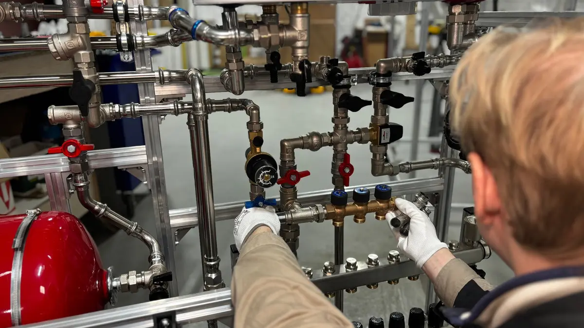 Engineer working on a pipework manifold beside a red expansion vessel