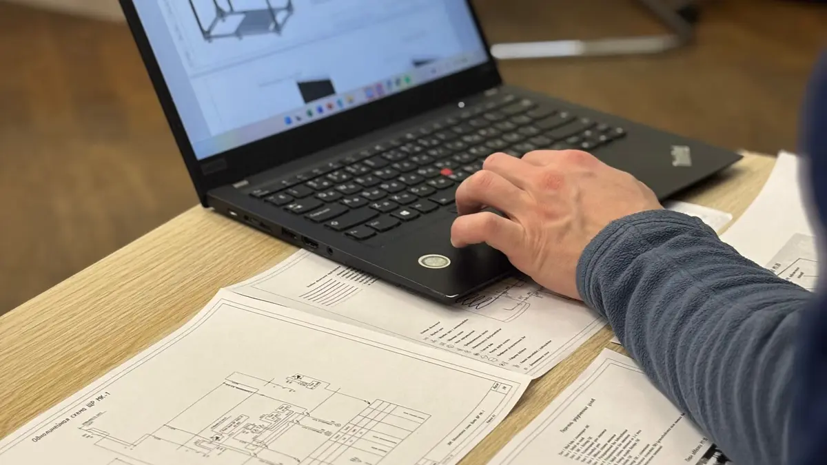 Engineer's hand on a laptop with plans on the desk