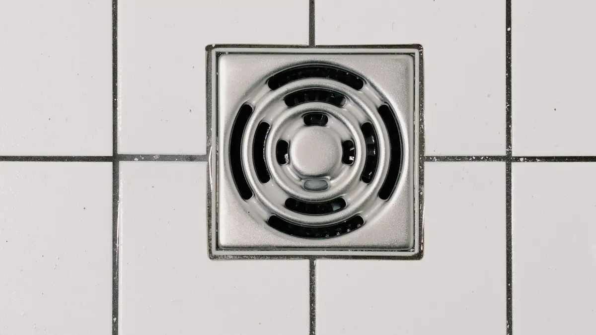 Square stainless steel drain cover in a white tiled shower